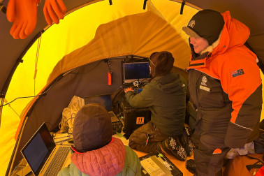 Dame Cindy observes the team at work inside tent with scientists at computers.