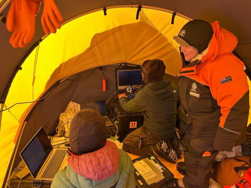 Dame Cindy observes the team at work inside tent with scientists at computers.