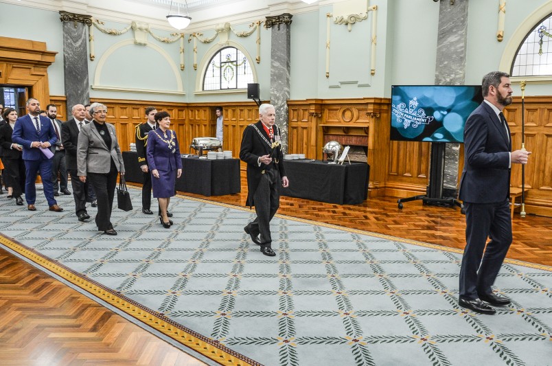 Image of Black Rod leads Dame Patsy and other dignitaries through the Grand Hall to the Legislative Council Chamber