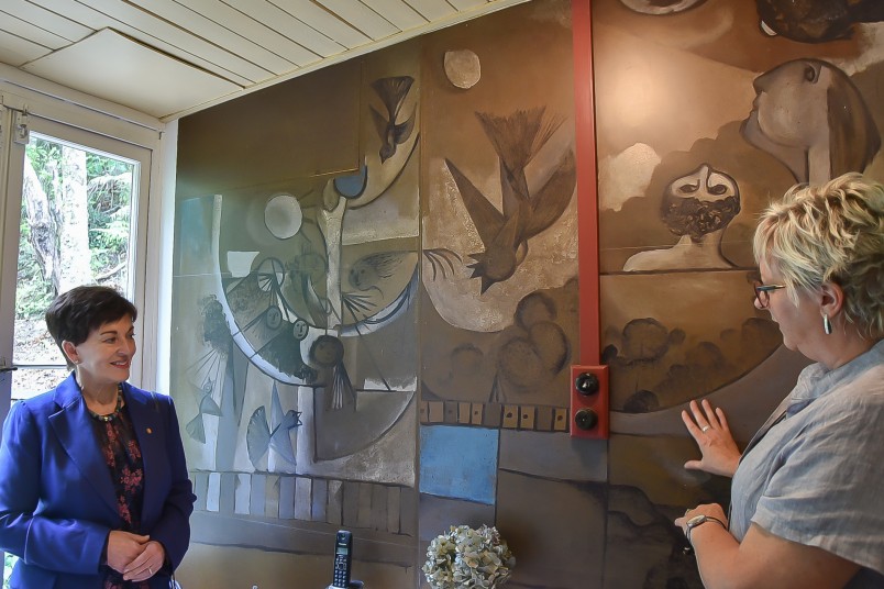 image of McCahon House Trust Chair Cynthia Smith taking Dame Patsy through the history of the mural in the kitchen