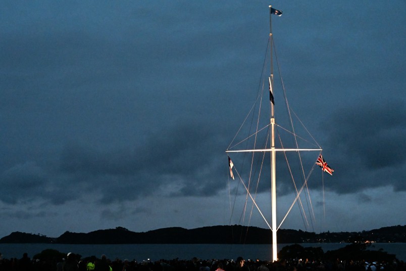 The Waitangi Flagstaff with dawn breaking over the Bay of Islands, the crowd gathered beneath