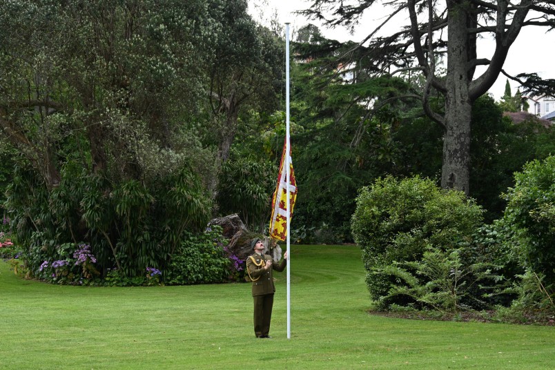 The Royal Standard is raised on the Government House lawn.