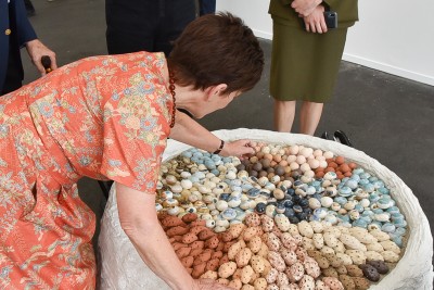 Image of Dame Patsy picking a clay form from Becky Richard's "An Egg, A Seed, A Stone"