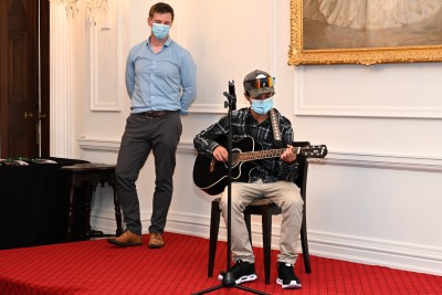 Zion Adler-Waititi playing guitar while his mentor looks on