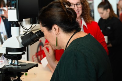 Dame Cindy inspecting a sample through a microscope